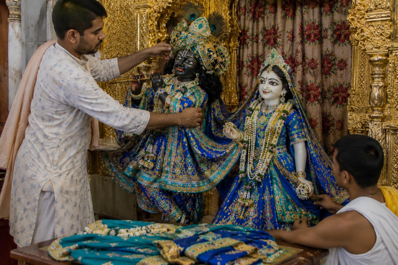 Pujaris draping the deities in blue vastra and poshak.